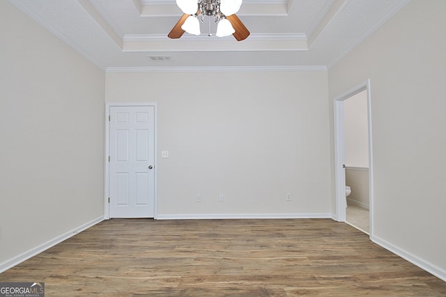 empty room featuring a tray ceiling, ceiling fan, crown molding, and wood-type flooring