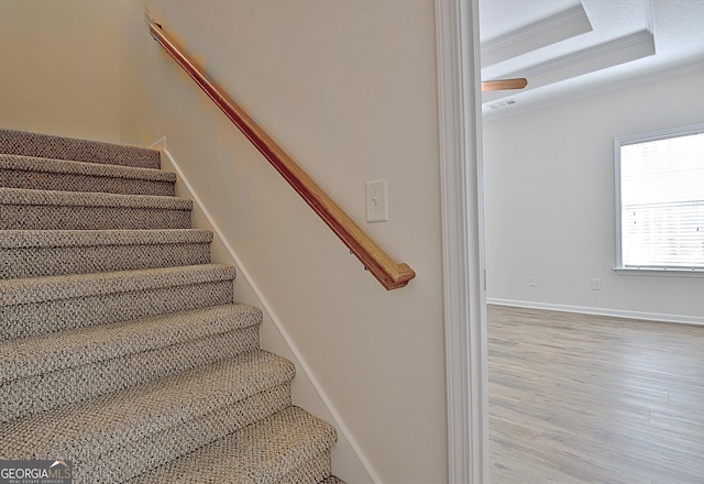 stairway featuring a raised ceiling, wood-type flooring, and crown molding