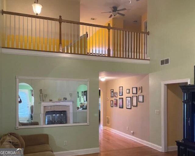 living room featuring a tile fireplace, wood-type flooring, ceiling fan, and a high ceiling