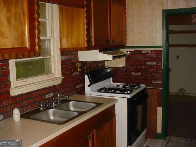 kitchen featuring light tile patterned flooring, sink, white gas range oven, and exhaust hood