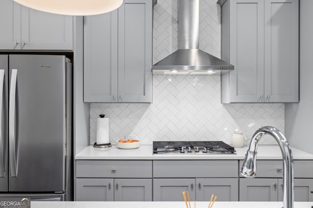 kitchen with gray cabinetry, wall chimney range hood, stainless steel appliances, and tasteful backsplash