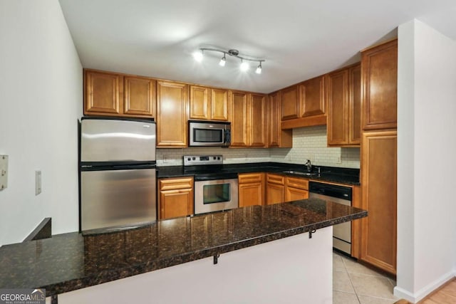 kitchen featuring sink, kitchen peninsula, dark stone countertops, decorative backsplash, and appliances with stainless steel finishes