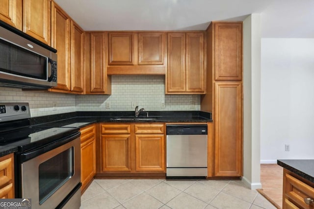 kitchen with dark stone countertops, sink, light tile patterned floors, and appliances with stainless steel finishes