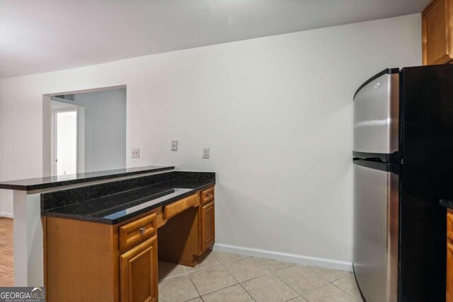 kitchen featuring kitchen peninsula, stainless steel fridge, dark stone counters, light tile patterned flooring, and built in desk