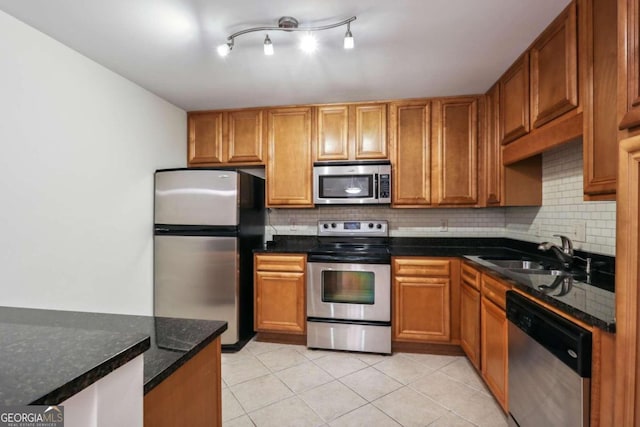 kitchen featuring dark stone counters, sink, light tile patterned floors, appliances with stainless steel finishes, and tasteful backsplash