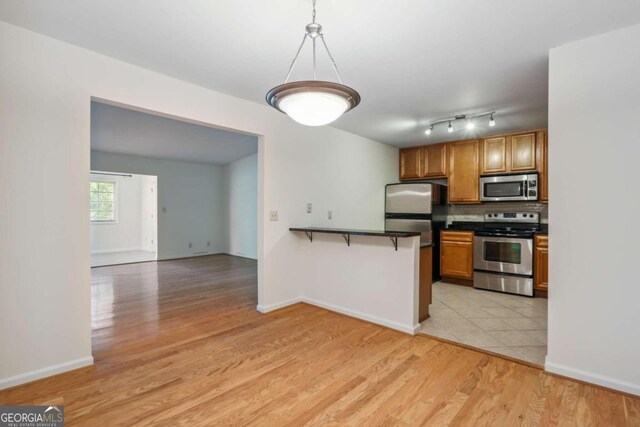 kitchen with hanging light fixtures, light hardwood / wood-style flooring, kitchen peninsula, a breakfast bar, and appliances with stainless steel finishes