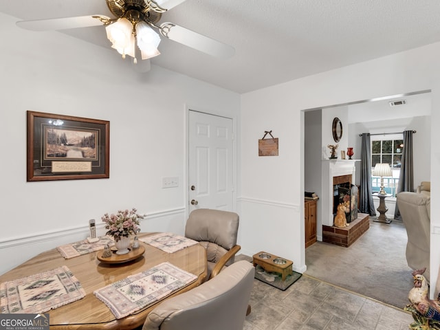 dining area with a fireplace, light colored carpet, and ceiling fan