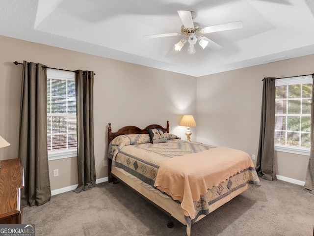 bedroom featuring a tray ceiling, multiple windows, ceiling fan, and carpet flooring