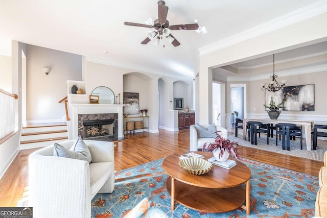 living room featuring hardwood / wood-style flooring, ceiling fan with notable chandelier, ornamental molding, and a high end fireplace