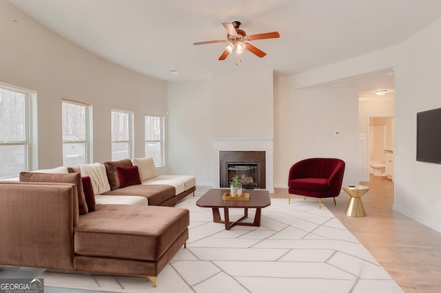 living room with a glass covered fireplace, baseboards, ceiling fan, and light wood finished floors