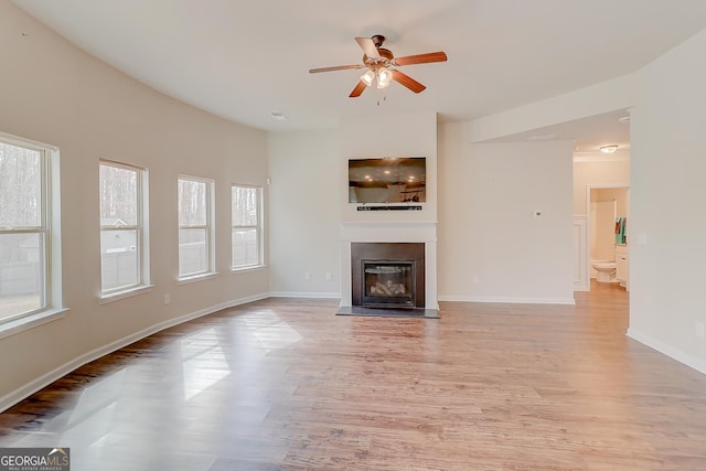 unfurnished living room with a ceiling fan, a glass covered fireplace, light wood-style flooring, and baseboards