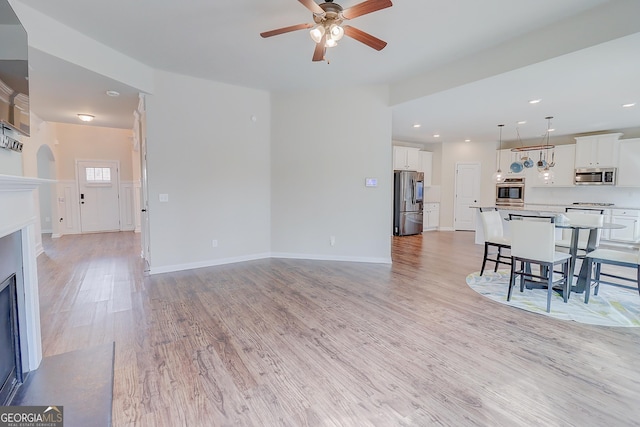 living area with light wood-type flooring, a fireplace with flush hearth, a ceiling fan, and baseboards