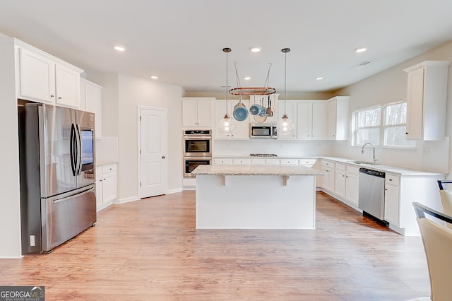 kitchen with stainless steel appliances, a kitchen island, white cabinets, and pendant lighting