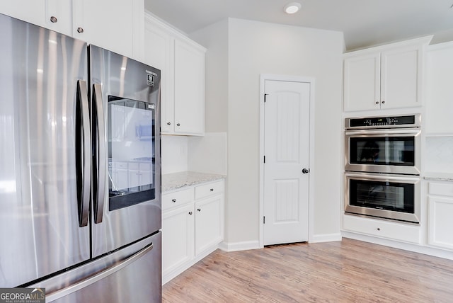 kitchen with stainless steel appliances, white cabinetry, and light stone countertops