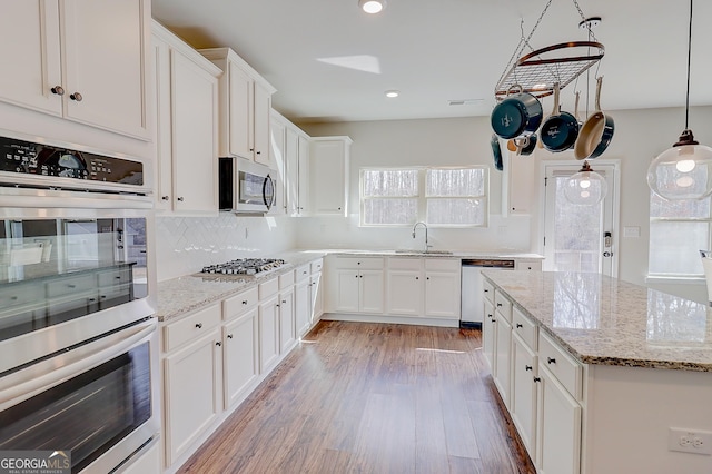 kitchen featuring light wood finished floors, white cabinets, a sink, stainless steel appliances, and backsplash