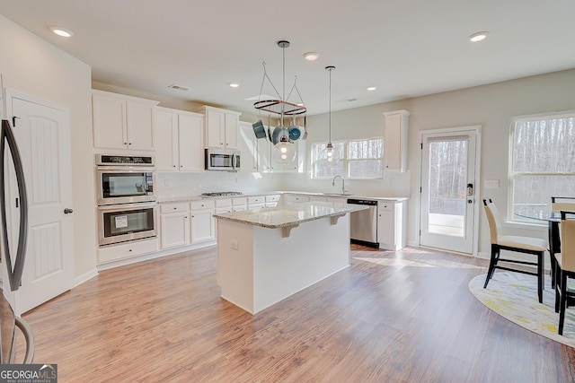 kitchen featuring stainless steel appliances, white cabinets, a kitchen island, and hanging light fixtures