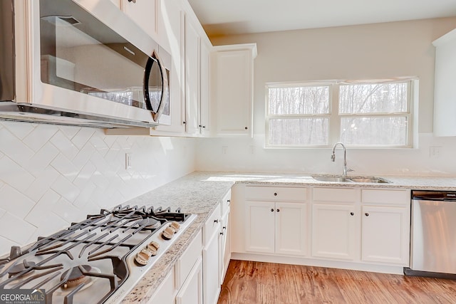 kitchen with light wood finished floors, white cabinets, light stone counters, appliances with stainless steel finishes, and a sink