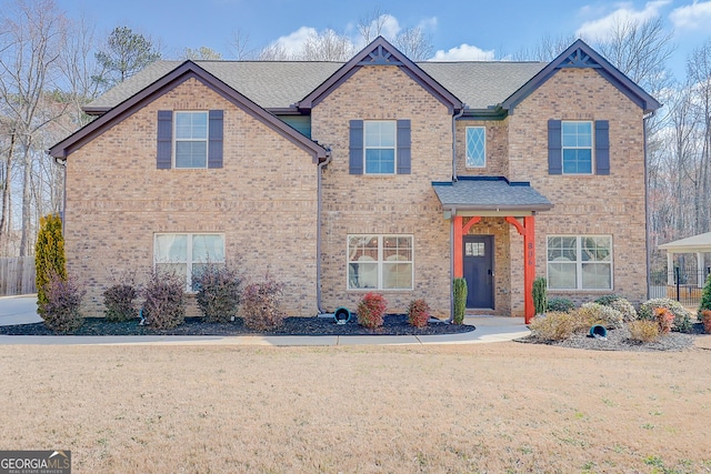 view of front of home with roof with shingles, brick siding, and a front lawn