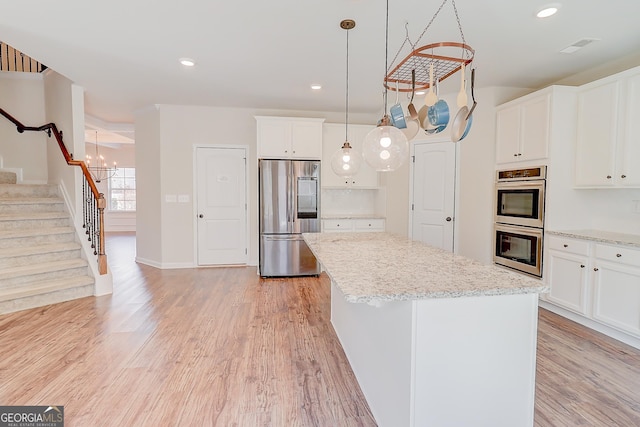 kitchen featuring decorative light fixtures, a center island, stainless steel appliances, light wood-type flooring, and white cabinetry