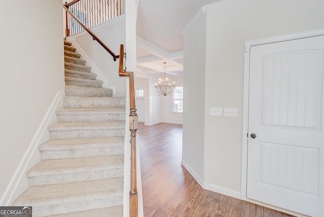 stairway with baseboards, coffered ceiling, wood finished floors, beamed ceiling, and an inviting chandelier