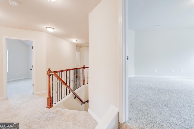 corridor featuring baseboards, attic access, an upstairs landing, and light colored carpet