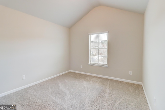 spare room featuring carpet, vaulted ceiling, and baseboards