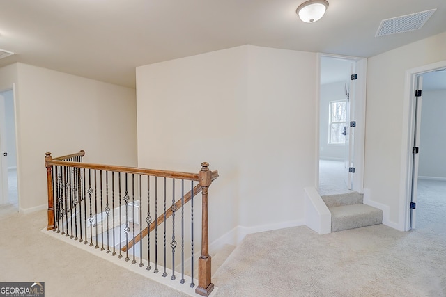 hall with carpet flooring, an upstairs landing, visible vents, and baseboards