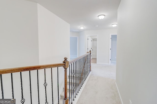 corridor featuring light carpet, baseboards, and an upstairs landing