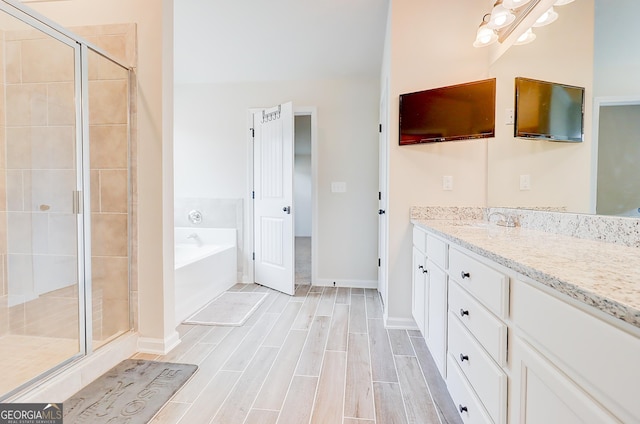 bathroom with a garden tub, wood finish floors, vanity, baseboards, and a stall shower