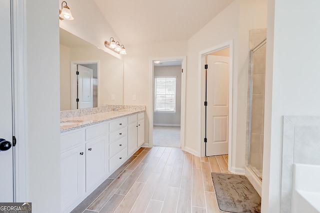 full bathroom featuring double vanity, baseboards, wood finished floors, a tile shower, and a sink