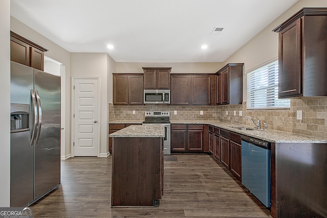 kitchen with a kitchen island, sink, dark brown cabinetry, stainless steel appliances, and light stone countertops