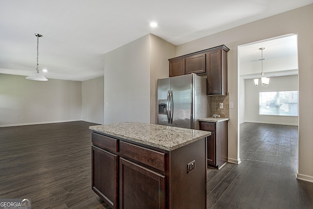 kitchen with stainless steel refrigerator with ice dispenser, dark brown cabinetry, a kitchen island, dark hardwood / wood-style flooring, and decorative light fixtures