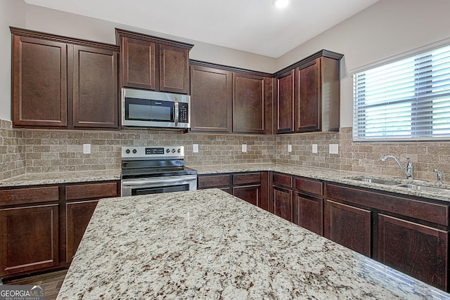 kitchen featuring tasteful backsplash, sink, dark brown cabinetry, light stone counters, and stainless steel appliances