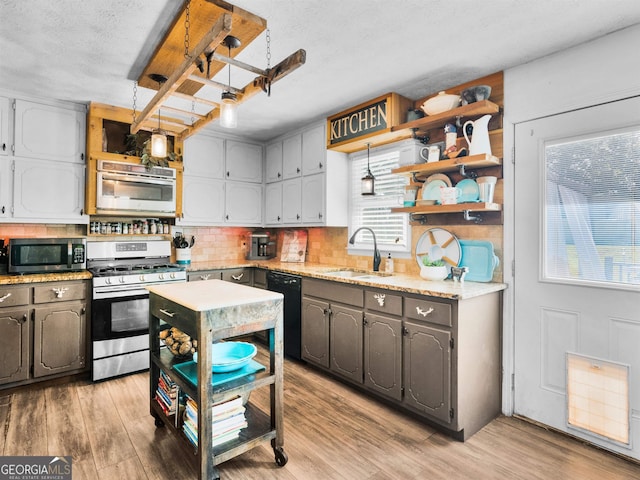 kitchen with open shelves, appliances with stainless steel finishes, a sink, and light wood-style flooring