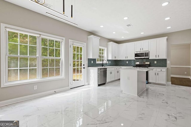 kitchen featuring white cabinets, decorative backsplash, a kitchen island, and appliances with stainless steel finishes