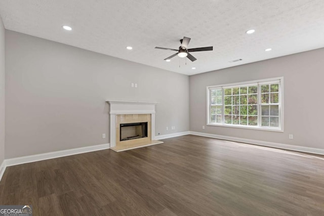 unfurnished living room featuring dark hardwood / wood-style flooring, a textured ceiling, ceiling fan, and a tiled fireplace