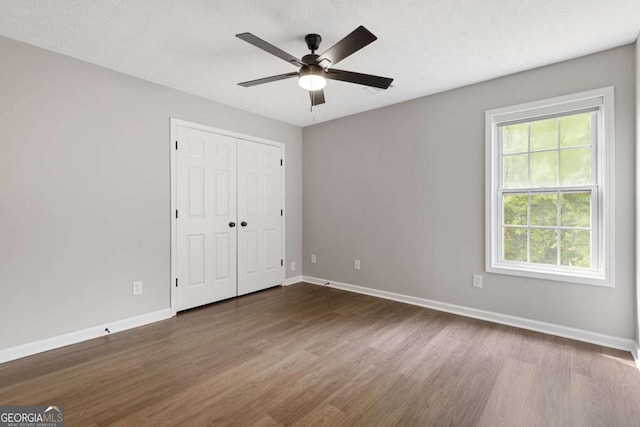 unfurnished bedroom featuring ceiling fan, a closet, dark wood-type flooring, and multiple windows