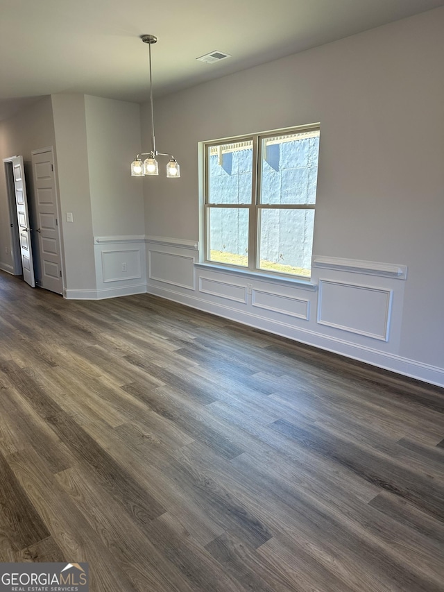 unfurnished dining area featuring dark wood-type flooring, a decorative wall, visible vents, and a notable chandelier