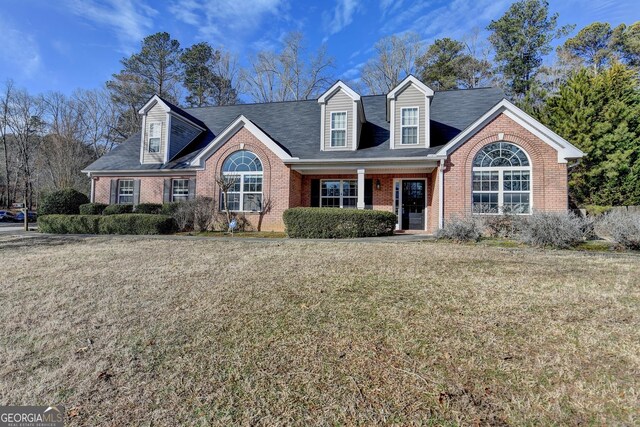 cape cod home featuring brick siding and a front lawn