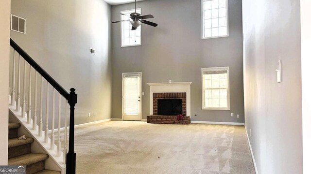 unfurnished living room featuring ceiling fan, a high ceiling, a brick fireplace, plenty of natural light, and carpet floors