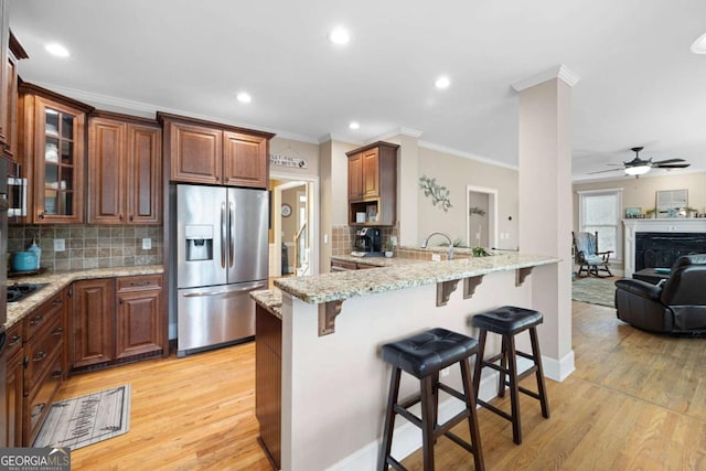 kitchen with kitchen peninsula, ceiling fan, decorative backsplash, a kitchen bar, and stainless steel fridge with ice dispenser