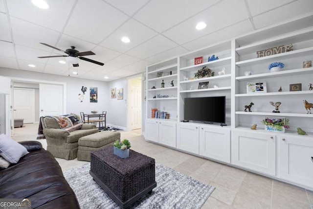 living room featuring built in shelves, a drop ceiling, and ceiling fan