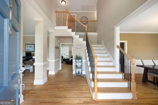 foyer entrance with a towering ceiling, light wood-type flooring, decorative columns, and crown molding