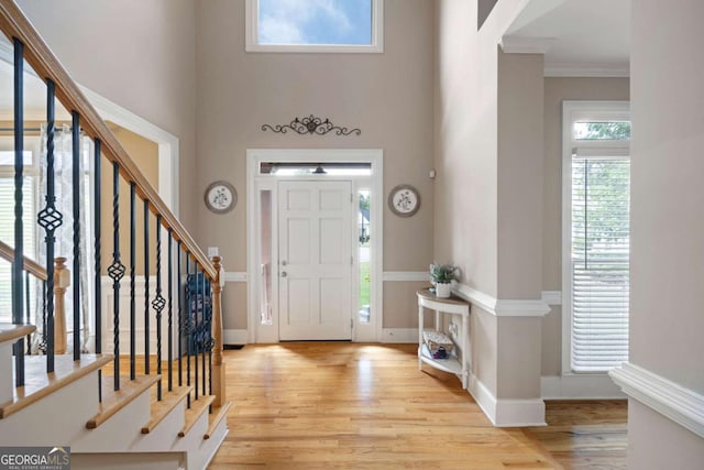 entryway featuring a towering ceiling, ornamental molding, and light wood-type flooring