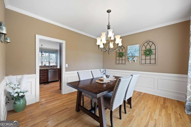 dining space with light wood-type flooring, ornamental molding, and an inviting chandelier