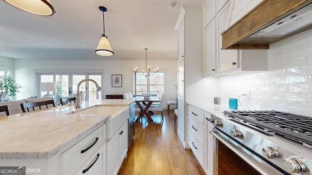 kitchen featuring white cabinets, an island with sink, decorative light fixtures, custom range hood, and stainless steel appliances