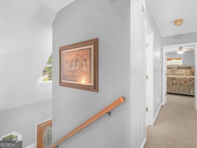 hall with a textured ceiling, light carpet, a healthy amount of sunlight, and vaulted ceiling