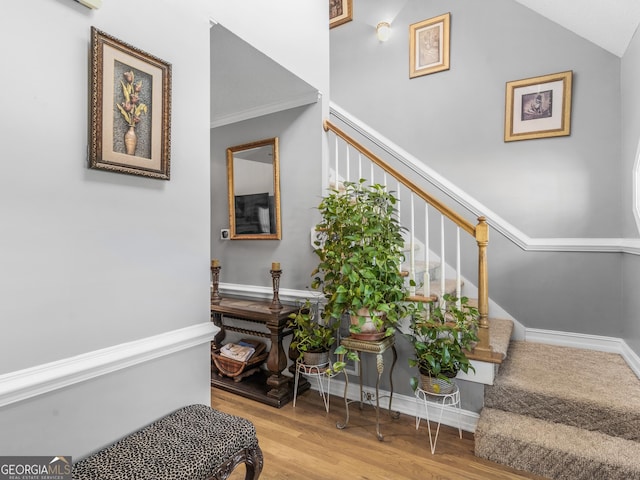 stairway featuring wood-type flooring, lofted ceiling, and ornamental molding