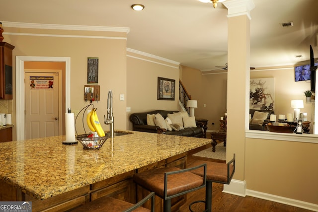 kitchen featuring sink, dark wood-type flooring, a kitchen breakfast bar, light stone counters, and crown molding