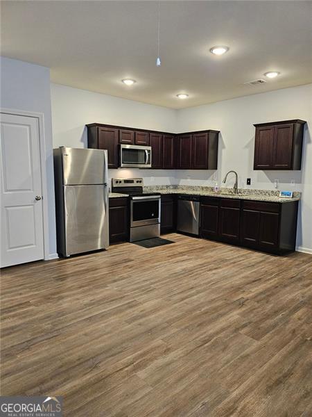 kitchen featuring dark brown cabinets, light stone counters, appliances with stainless steel finishes, and light hardwood / wood-style flooring